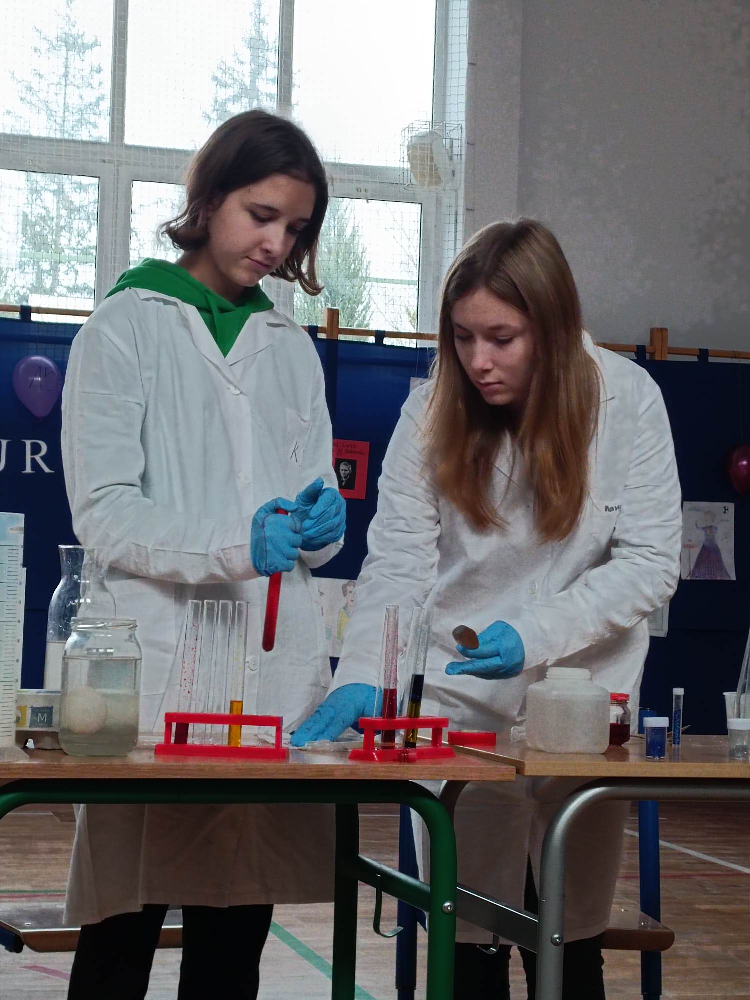 Dziewczynki w białych fartuchach wykonują doświadczenia chemiczne.