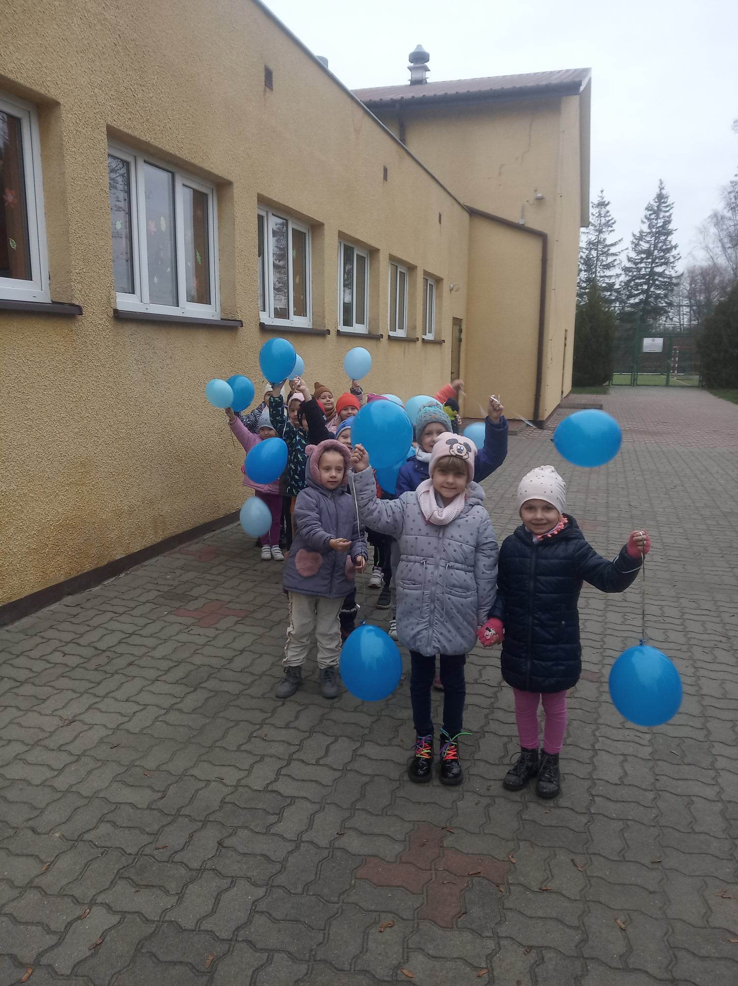 Dzieci machają niebieskimi balonami.